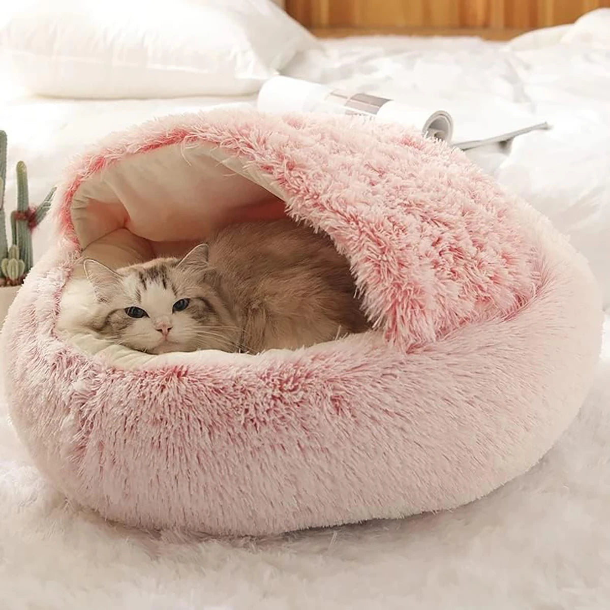 A cozy pink hooded cat bed with a cat sleeping inside. The bed provides a warm and secure space for cats to relax and unwind.