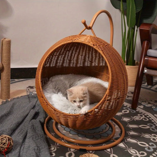 A cozy rattan cat swing bed with a fluffy cushion and a contented kitten curled up inside. The swing bed is suspended from a sturdy metal frame with a double-disc base.